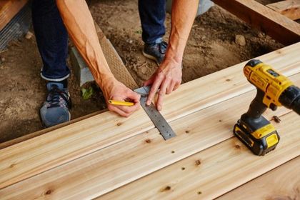 Measuring a wooden plank with a ruler and pencil beside a yellow drill on a worksite