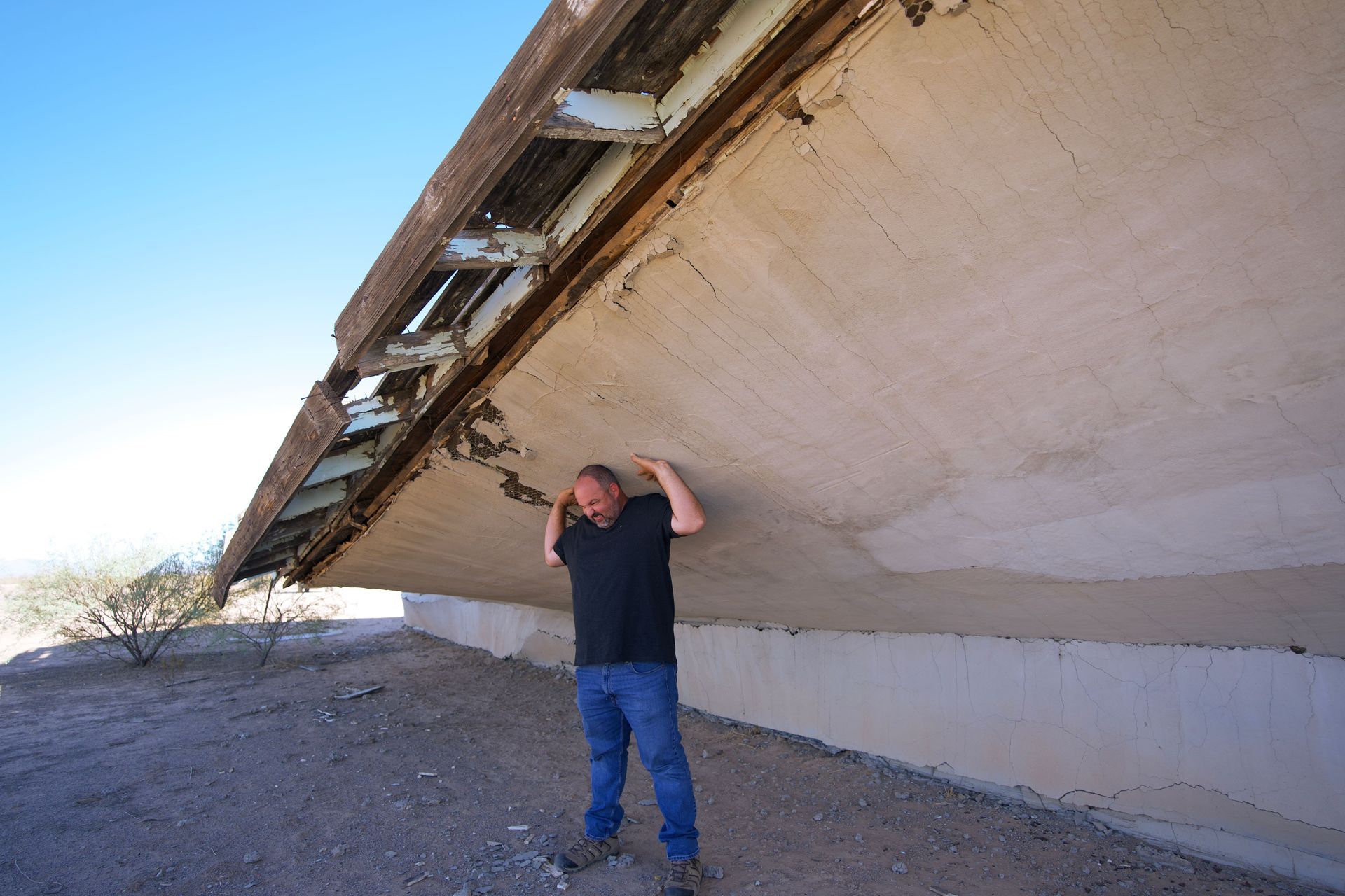 Person holding up a tilted concrete structure outdoors under a clear sky