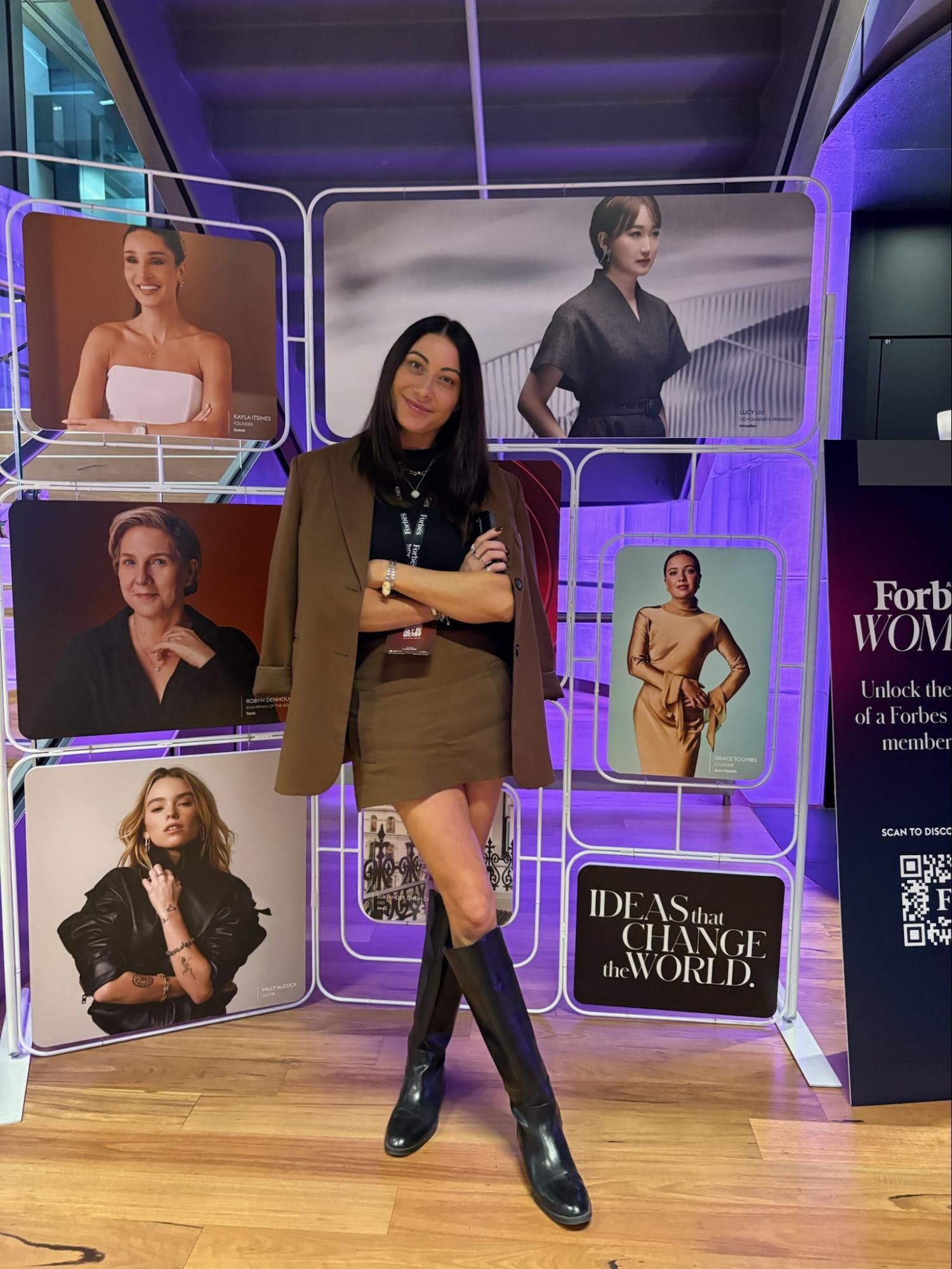 A woman standing in front of the Forbes Women Summit speaker wall.