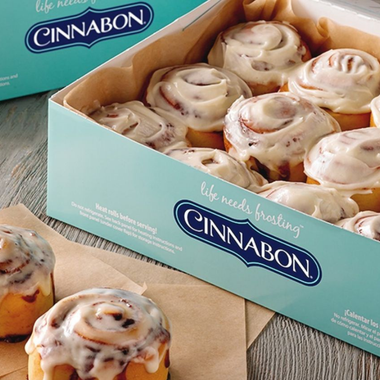 Cinnabon box of frosted cinnamon rolls on a table, with one roll partially visible in front