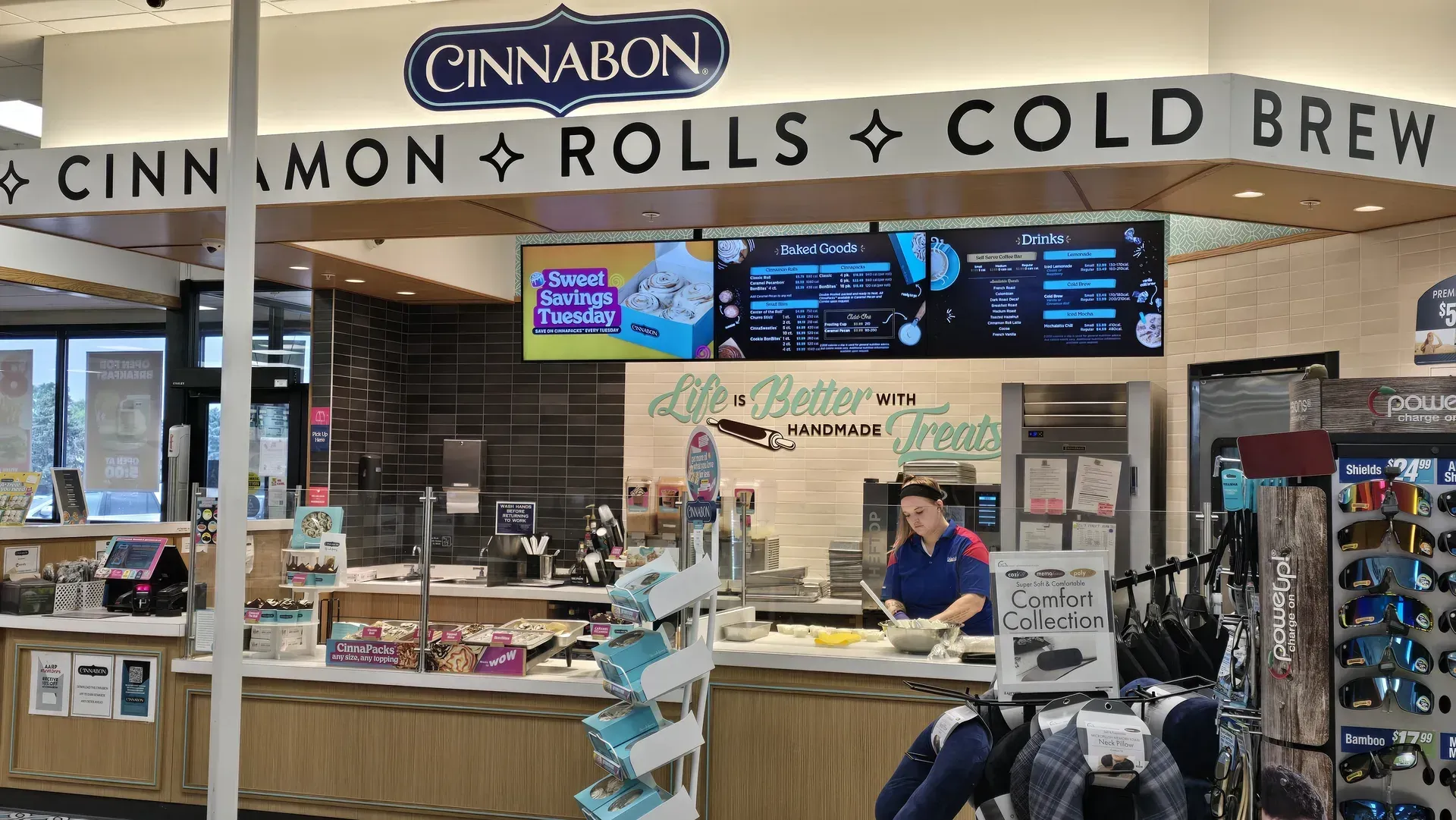 Cinnabon counter with menu boards, staff behind the counter, and a sign advertising cinnamon rolls and cold brew