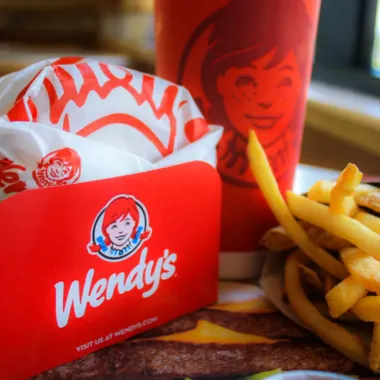 Wendy’s bag, fries, and drink on a table with a burger in the foreground