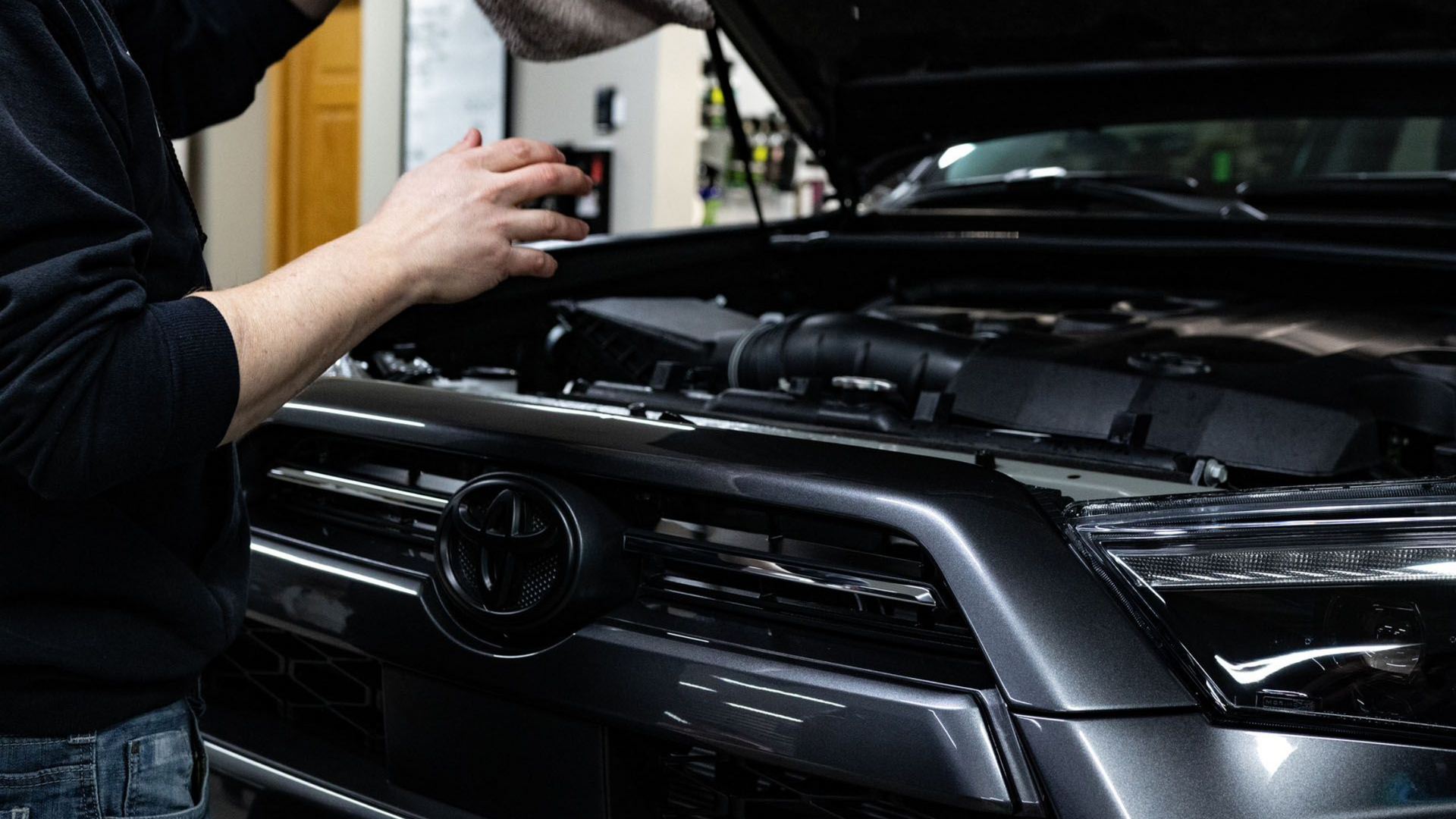 Person cleaning the front grille of a black Volkswagen in a garage