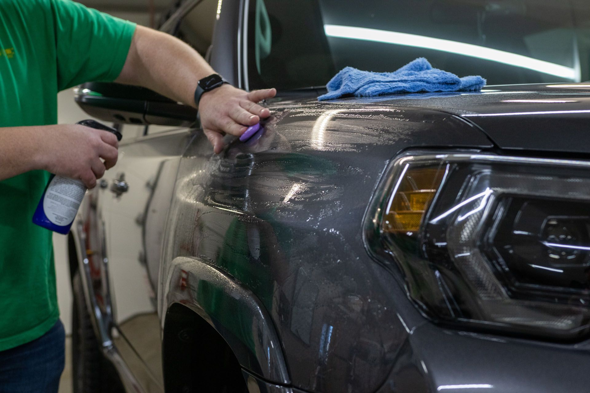 Person cleaning a black truck with a cloth and spray bottle in a garage