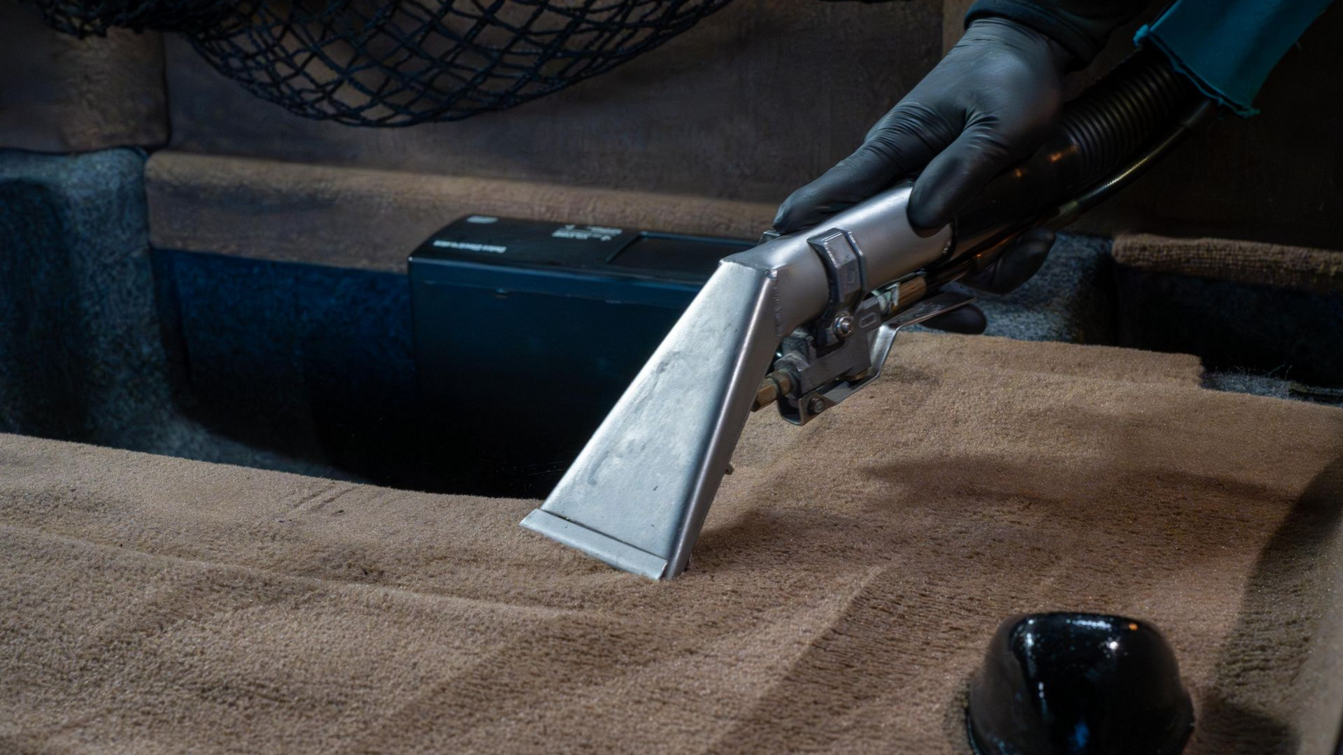 Handheld vacuum nozzle cleaning beige carpet near a dark shoe