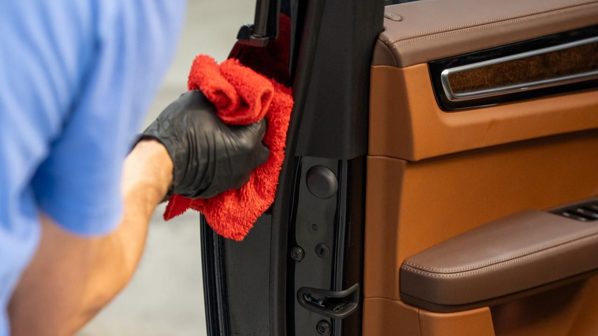 Person wiping a car door with a red cloth and black glove
