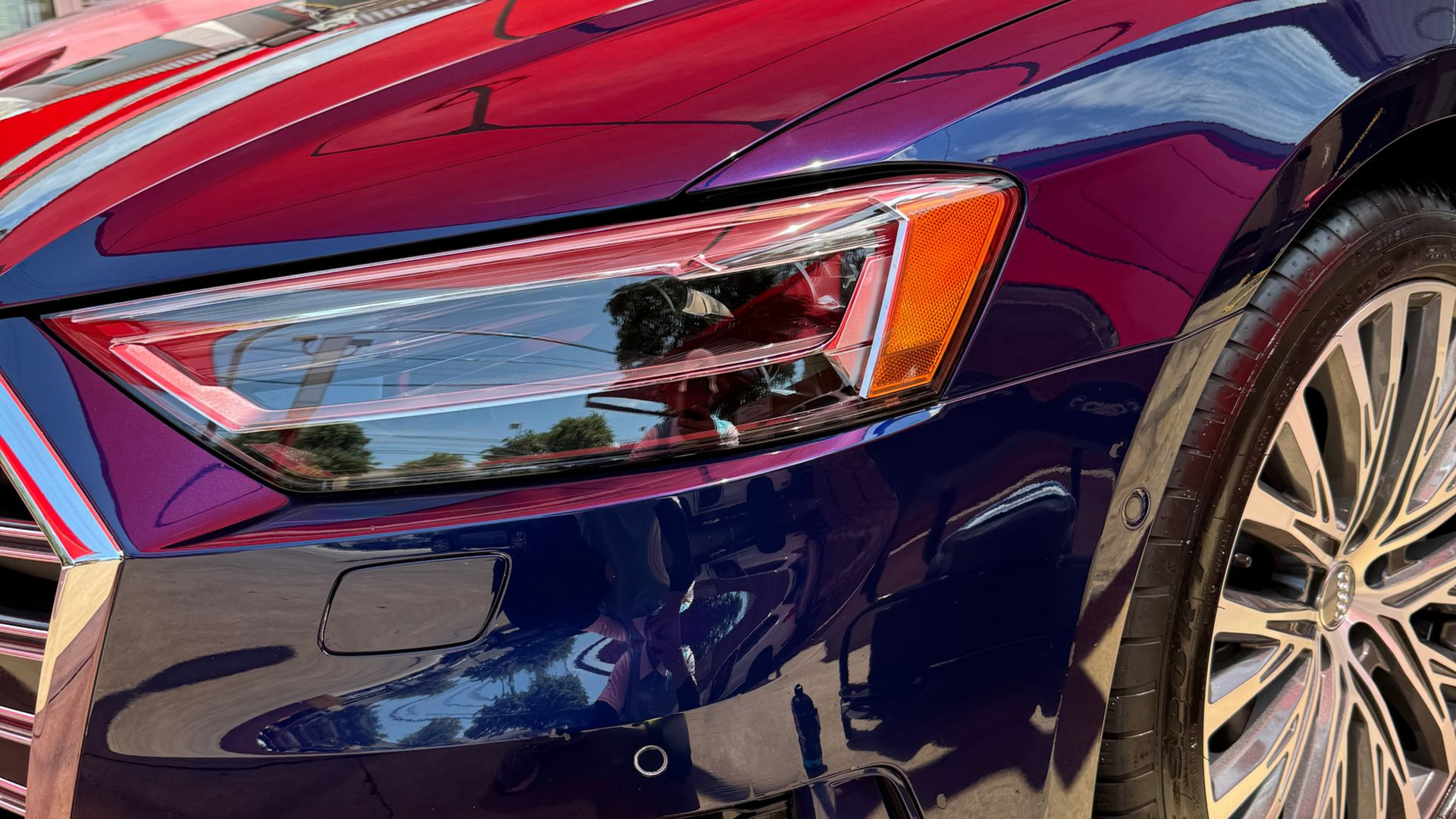 Close-up of a purple car’s front headlight and wheel in sunlight
