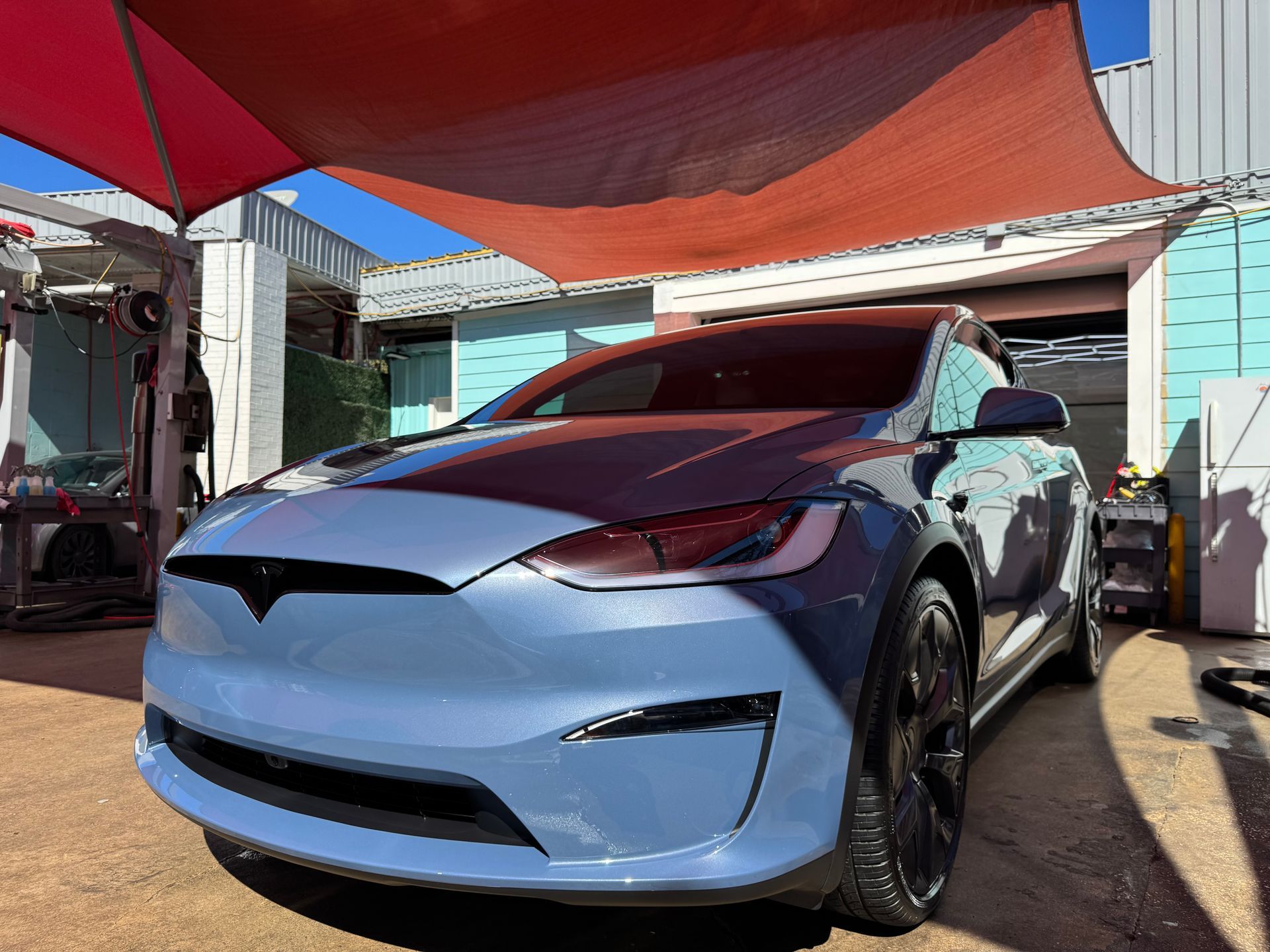 Light blue SUV parked under a red canopy in a sunny driveway