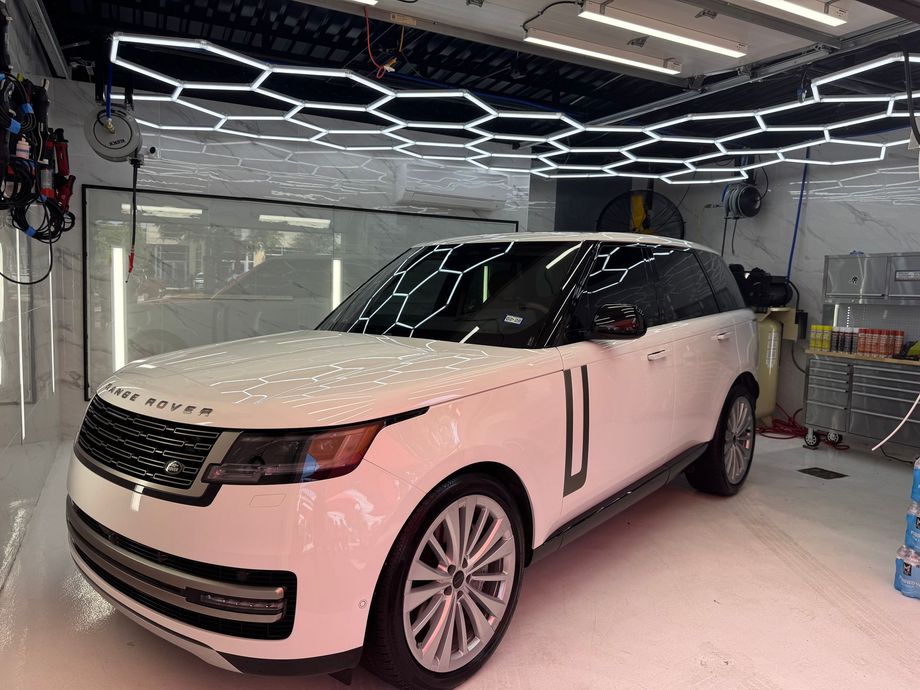 White Range Rover SUV in a garage under bright hexagonal ceiling lights.