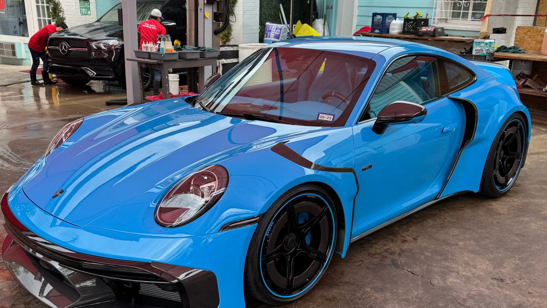 Bright blue sports car with black rims parked outdoors in a wet lot