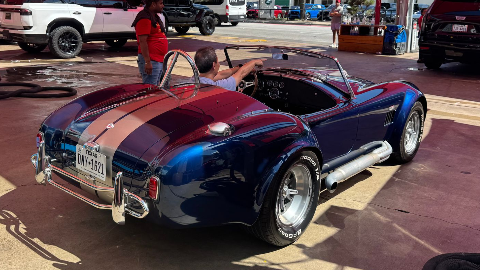 Blue classic Shelby Cobra convertible with red racing stripes parked outdoors