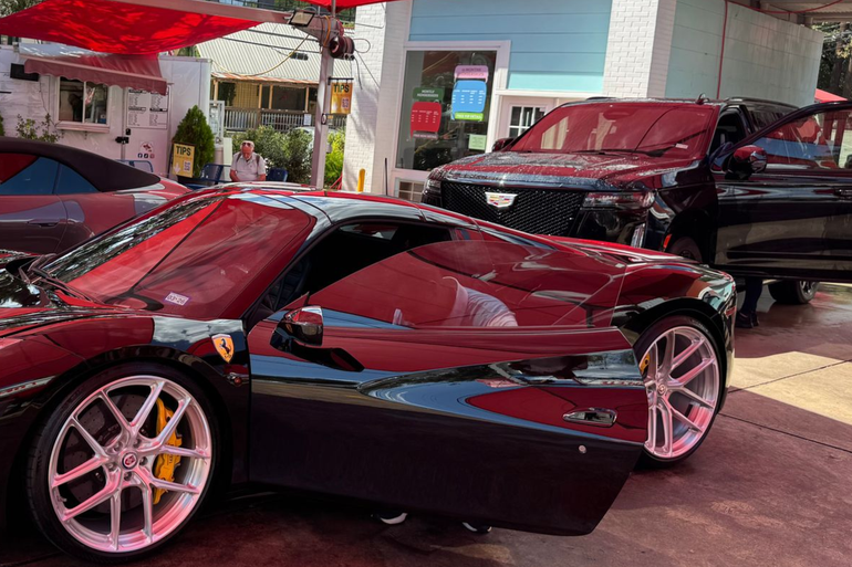 Red sports car with scissor door open at an outdoor showroom, with a black car behind it.
