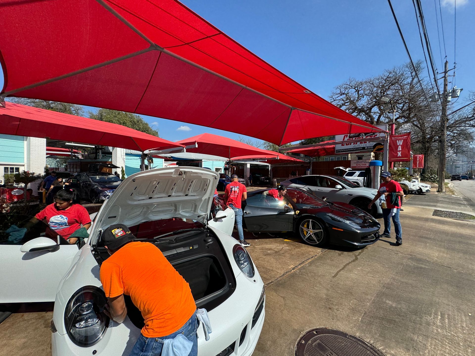 People inspecting sports cars under red canopies at an outdoor car show