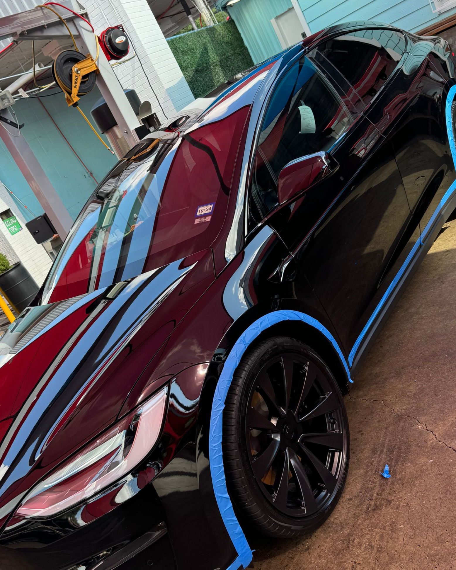 Maroon sedan being detailed outdoors, with blue protective tape around the body and black wheels