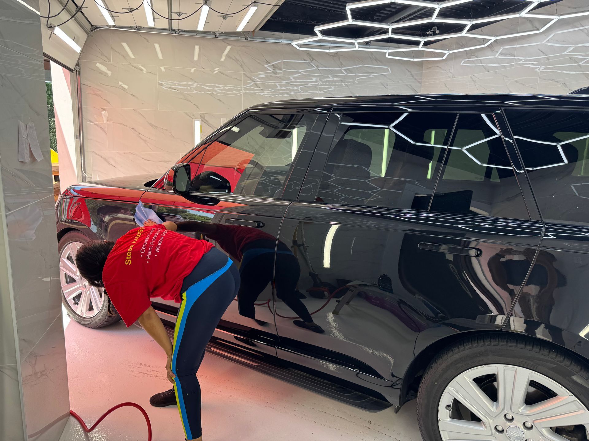 Person polishing a black car in a garage, using a cloth near the front door.