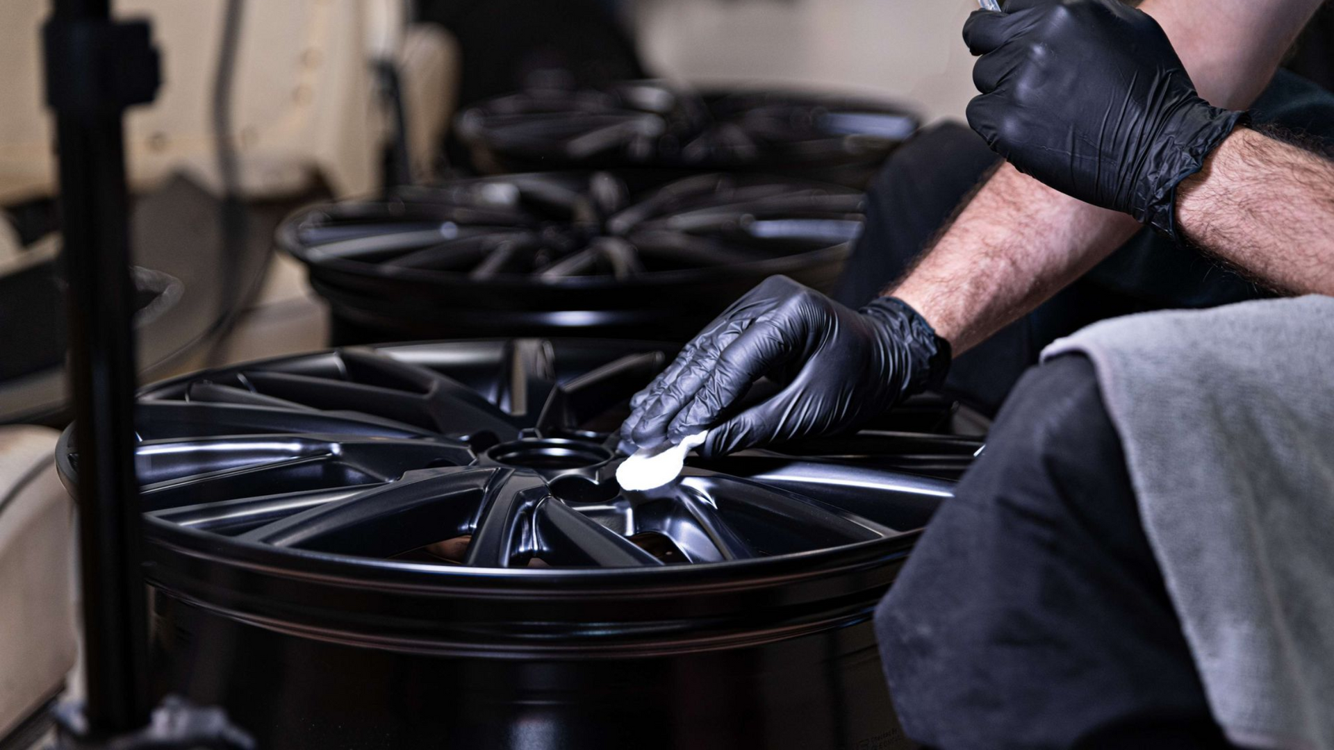 Gloved hands inspecting a black alloy wheel in a workshop
