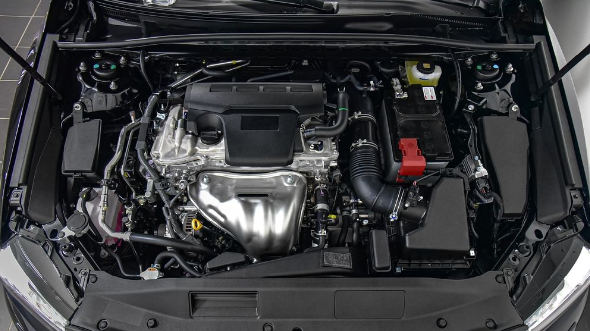 Car engine bay with a silver engine cover and red battery terminal, viewed from above