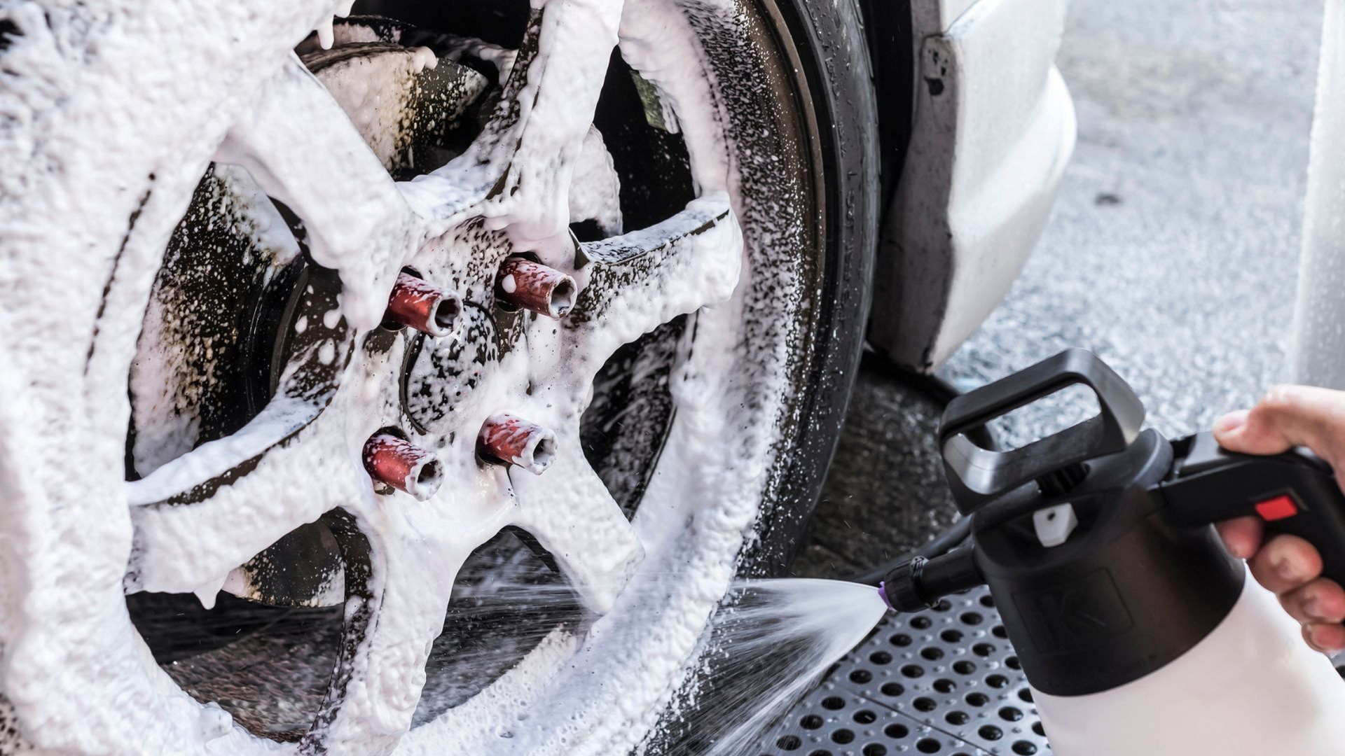 Person pressure-washing a snow-covered car wheel and tire with a spray nozzle