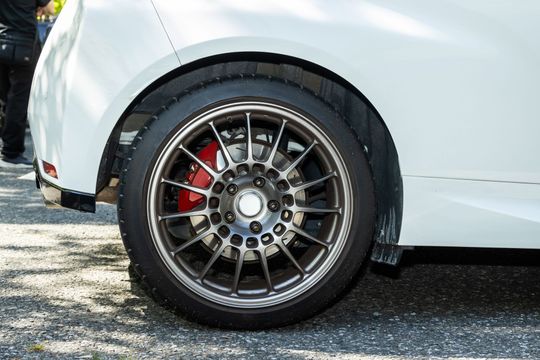Close-up of a white car’s rear wheel with black alloy rim and red brake caliper