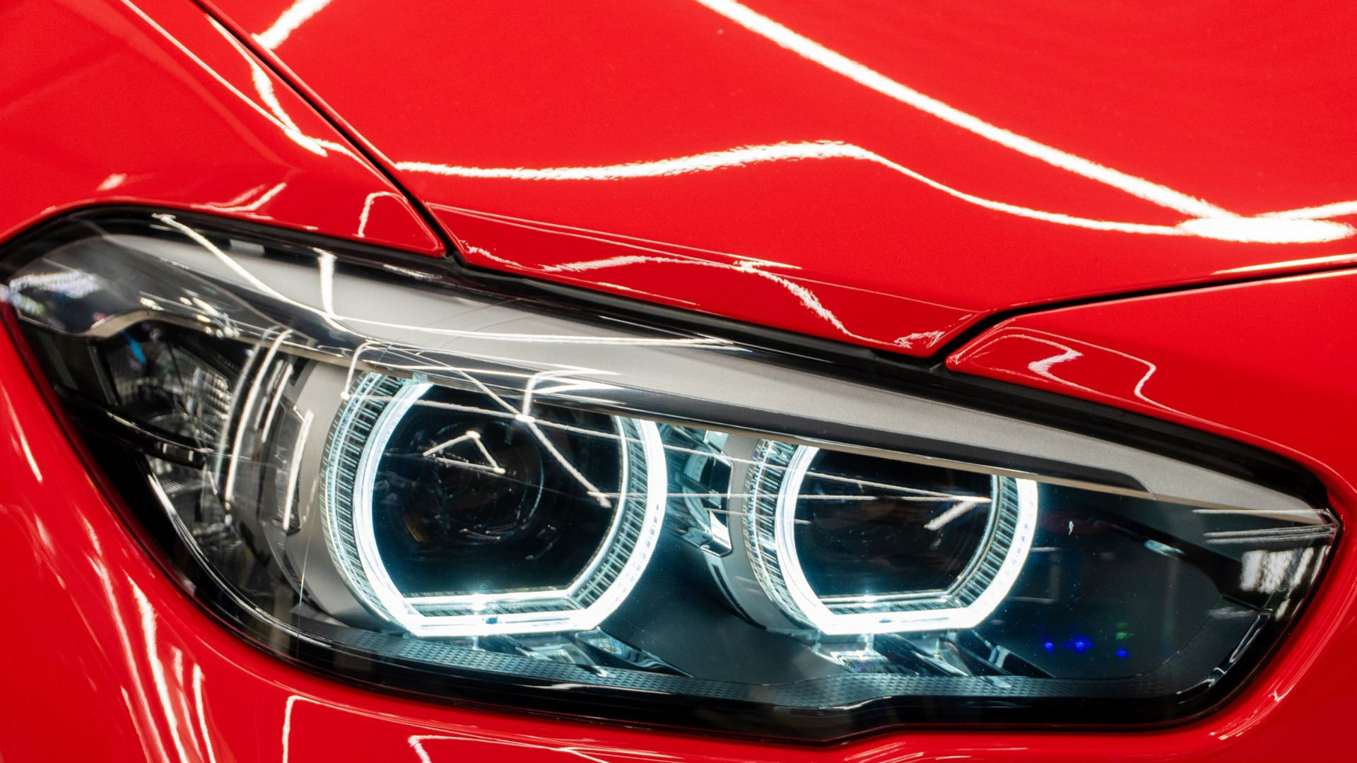 Close-up of a red car headlight with bright LED rings in a glossy black housing