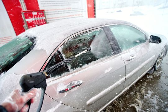 Silver car being washed with soapy foam in a car wash bay