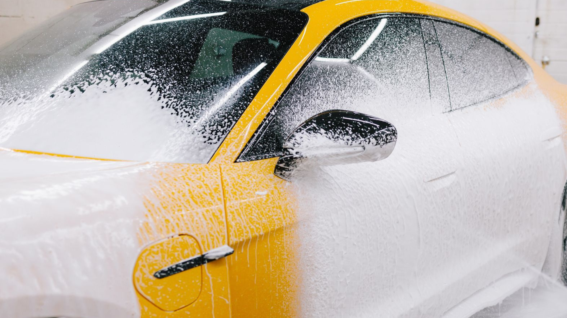 Yellow sports car being washed with thick white foam and spray.