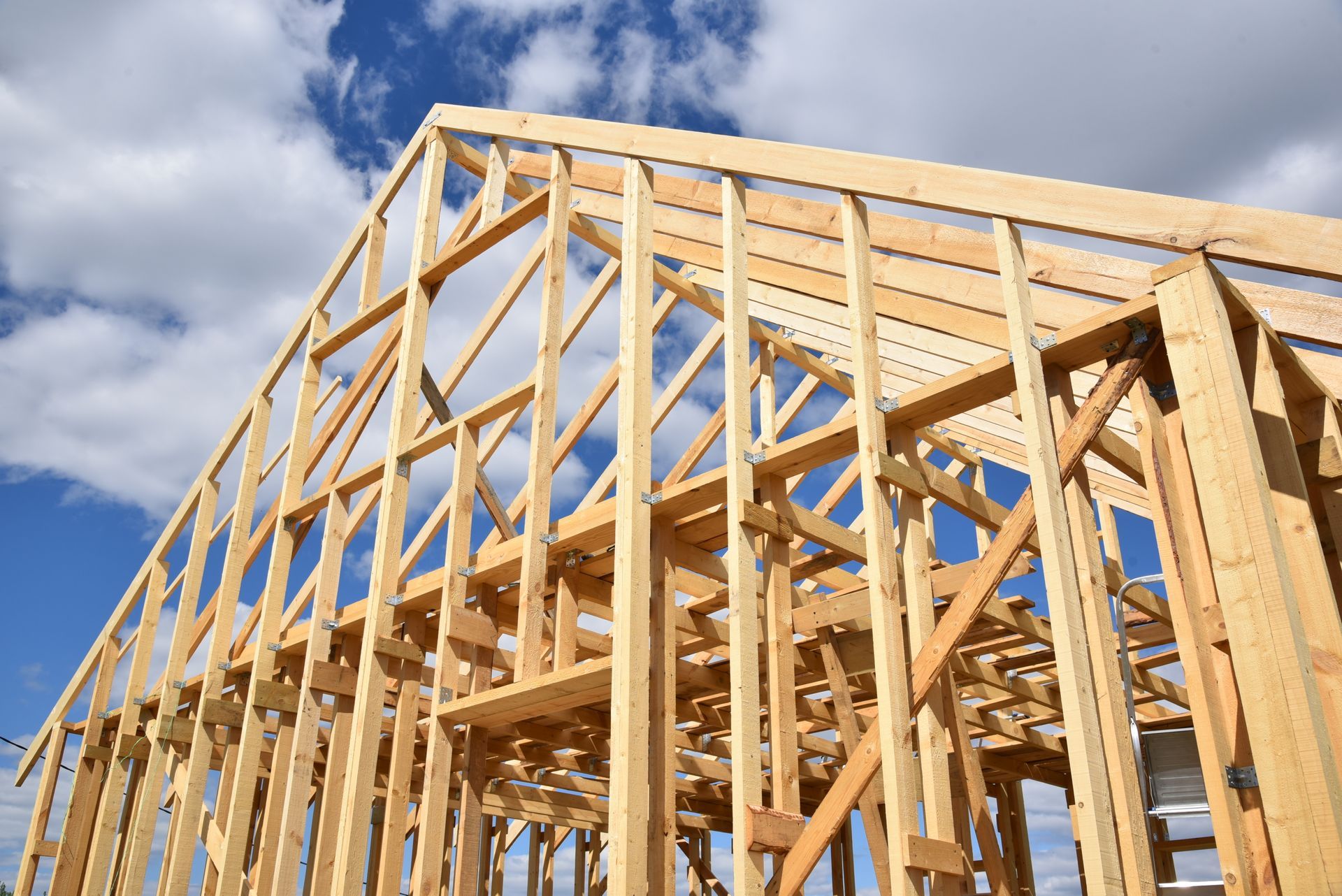 Ossature en bois d'une maison en construction contre un ciel bleu avec des nuages.