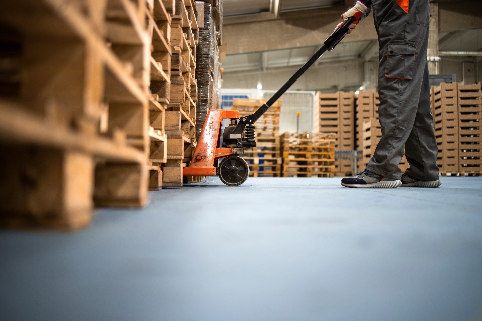 Low angle view of unrecognizable worker lifting palette with manual forklift.