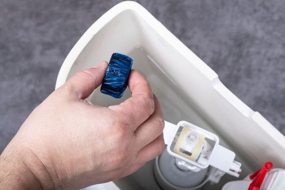 a person putting a cleaning tablet in the toilet tank