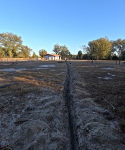 A dirt path runs through a dry field toward a small house under a clear blue sky.