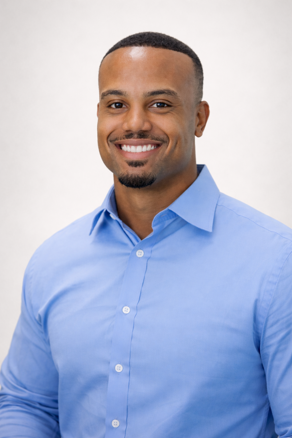 A smiling person wearing a light blue button-down shirt, posed against a neutral, plain background.