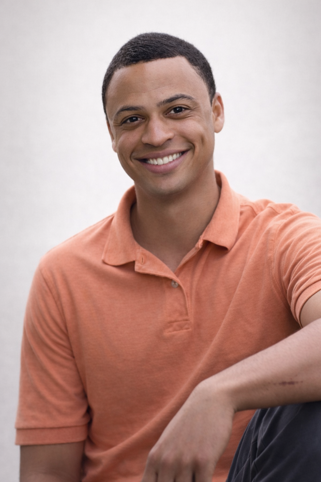 A smiling person in a peach-colored polo shirt against a plain, light-colored background.