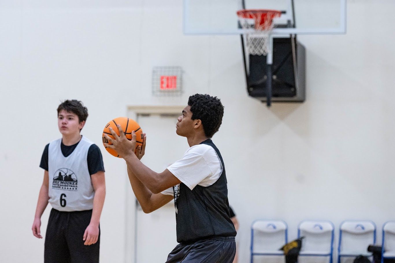 A basketball player in a dark jersey prepares to shoot a ball on an indoor court while a teammate stands nearby.