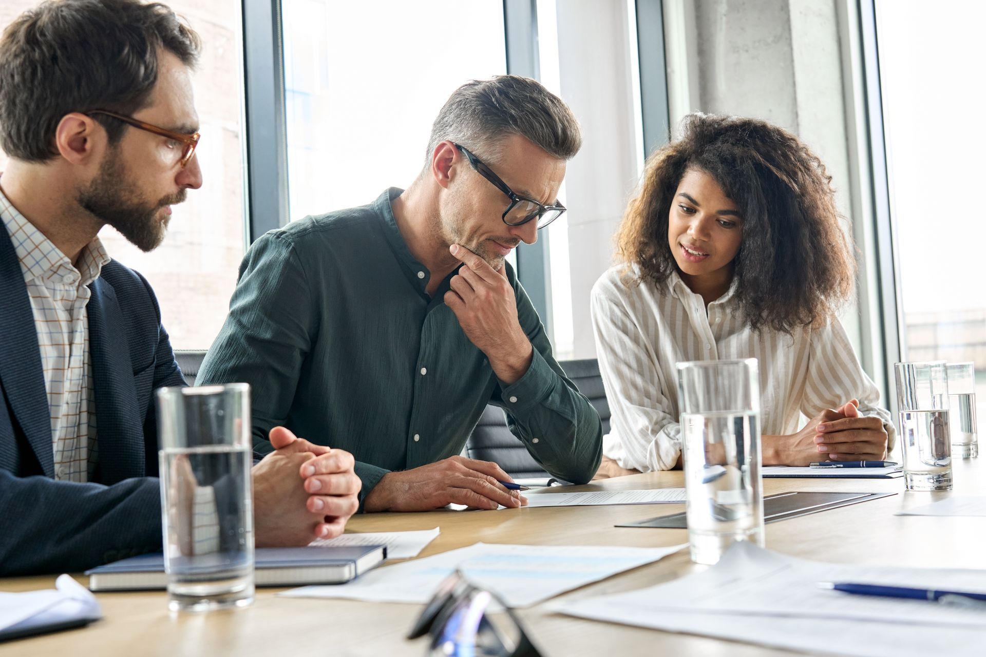 Three coworkers in a meeting, reviewing documents at a table with water glasses and papers.