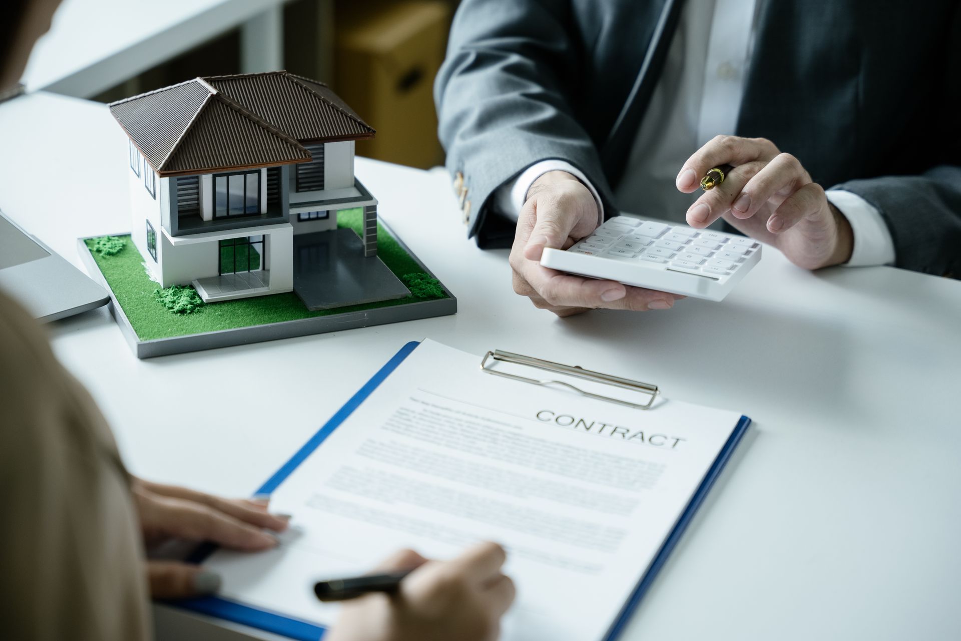 Hands exchanging a document over a contract on a desk beside a house model