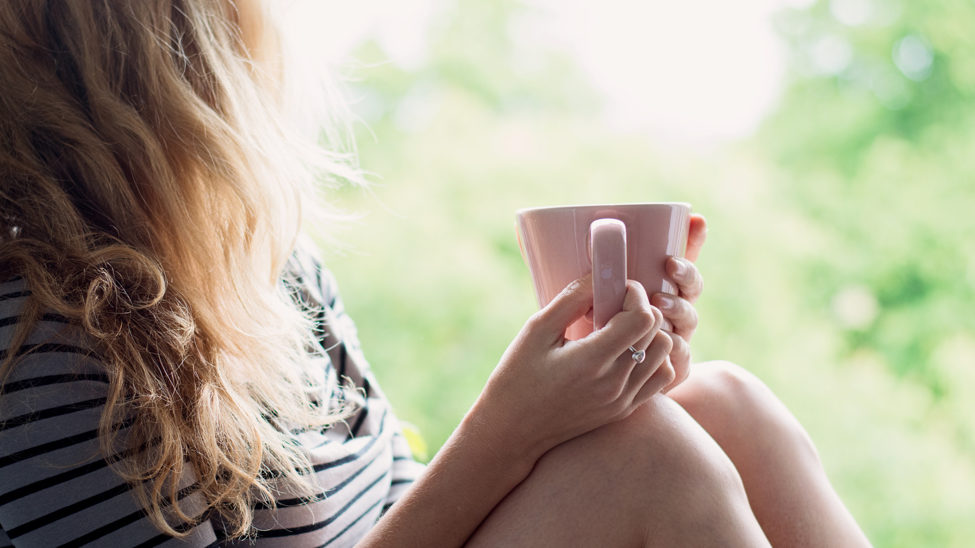 A woman is sitting on a window sill holding a cup of coffee.