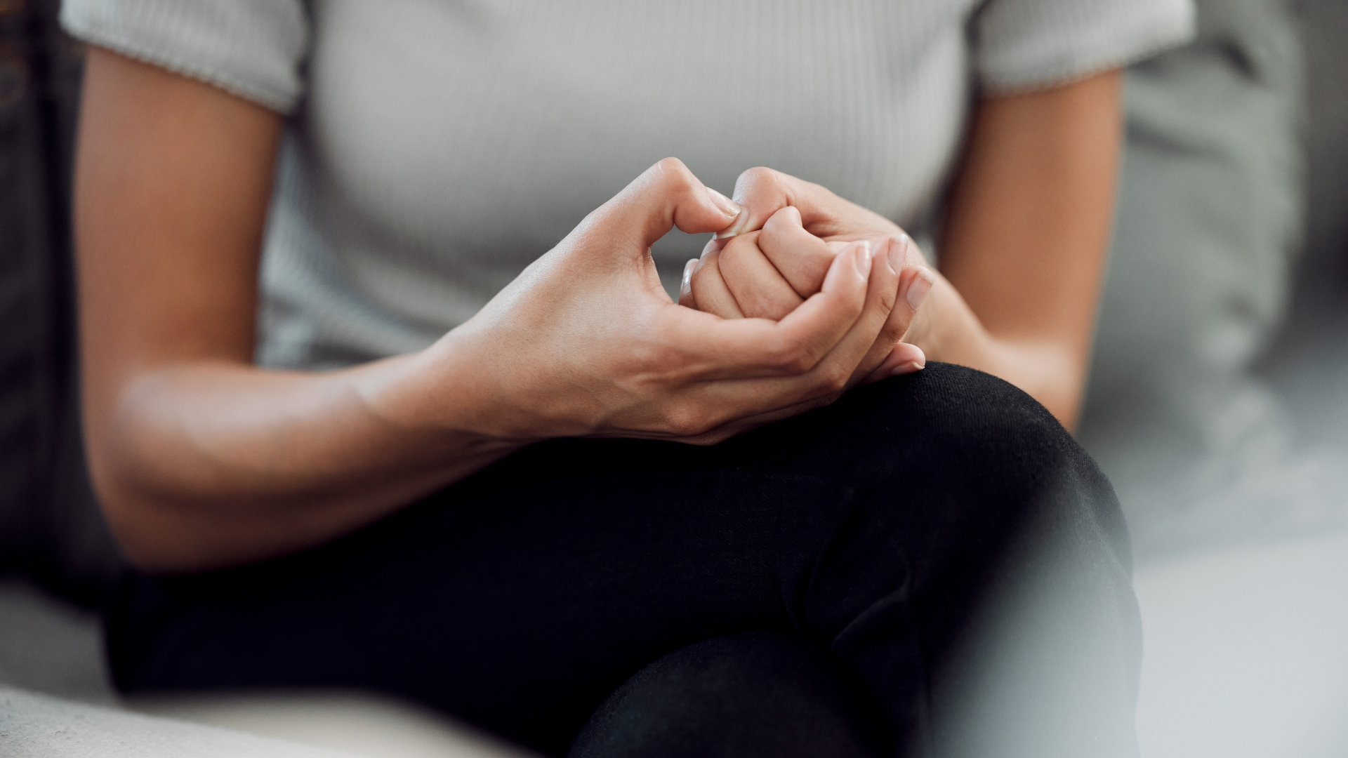 A woman is sitting on a couch with her hands folded in a heart shape.