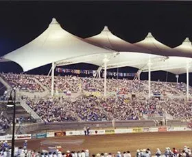 Packed grandstands at a nighttime stadium under white canopy roofs, with a track in the foreground