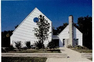 White house with a tall chimney, round window, and a walkway under a blue sky