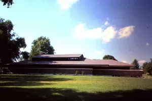 Low brick building with dark roof in a sunny grassy field under a blue sky