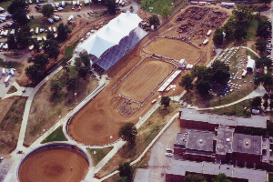 Aerial view of an outdoor rodeo arena with a large white tent and surrounding buildings.