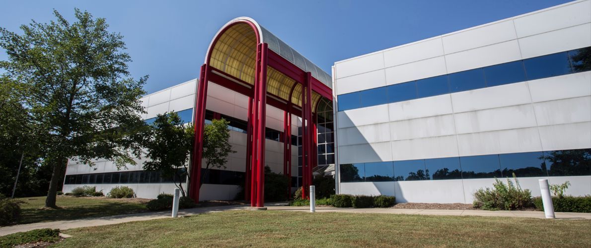 Modern office building with red arch entrance and blue-tinted glass windows under a clear sky