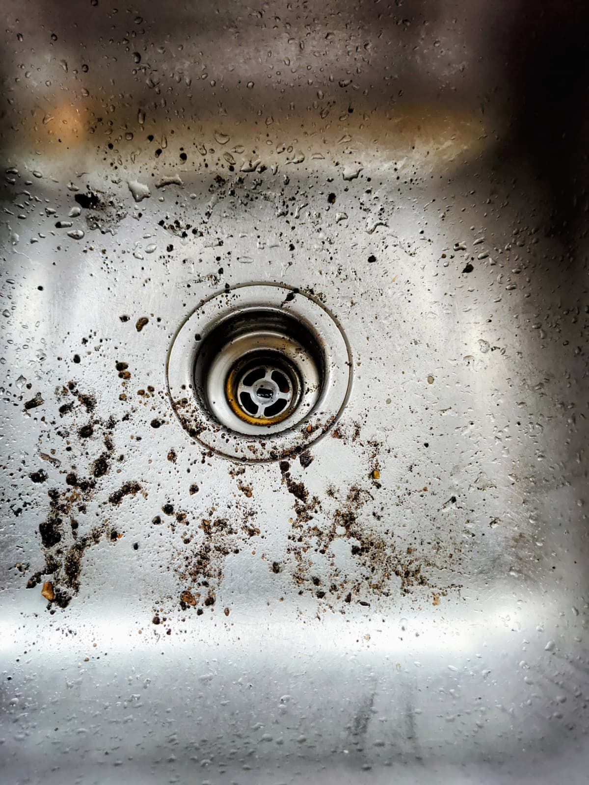 Dirty stainless steel sink drain with grime and debris around the basin