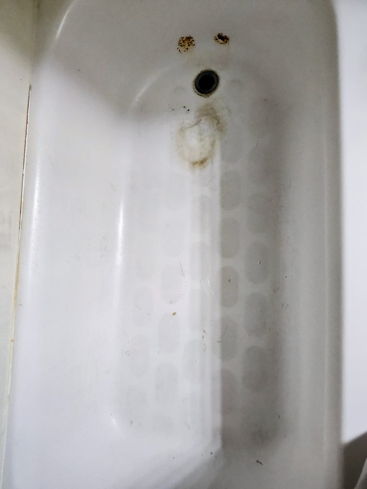 White bathtub drain with rust stains and grime near the overflow hole.
