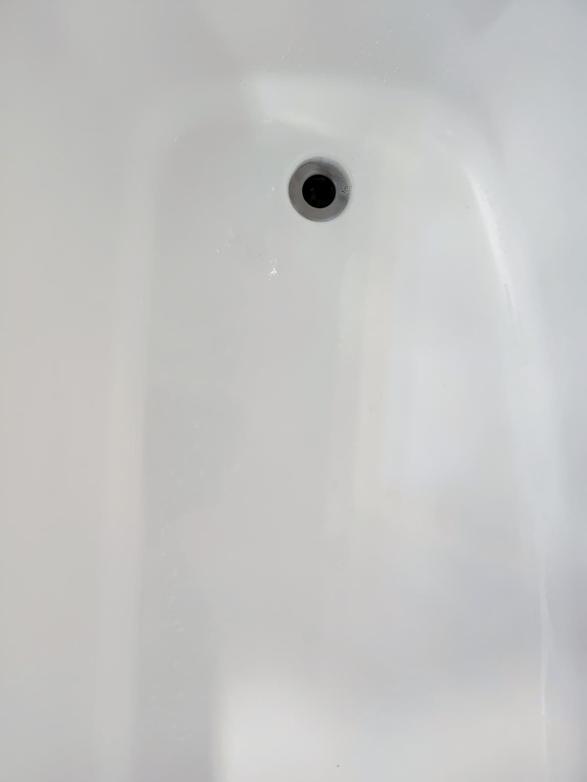 White bathtub wall with a drain hole near the top center.