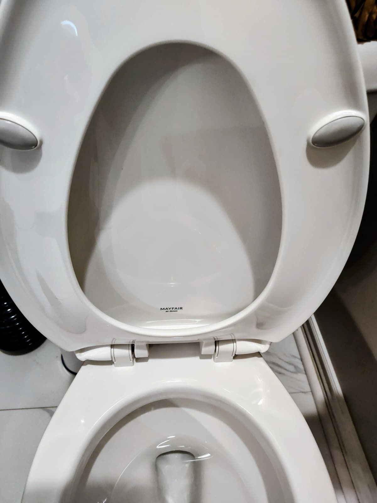 Open toilet seat in a restroom, showing the bowl and white porcelain.
