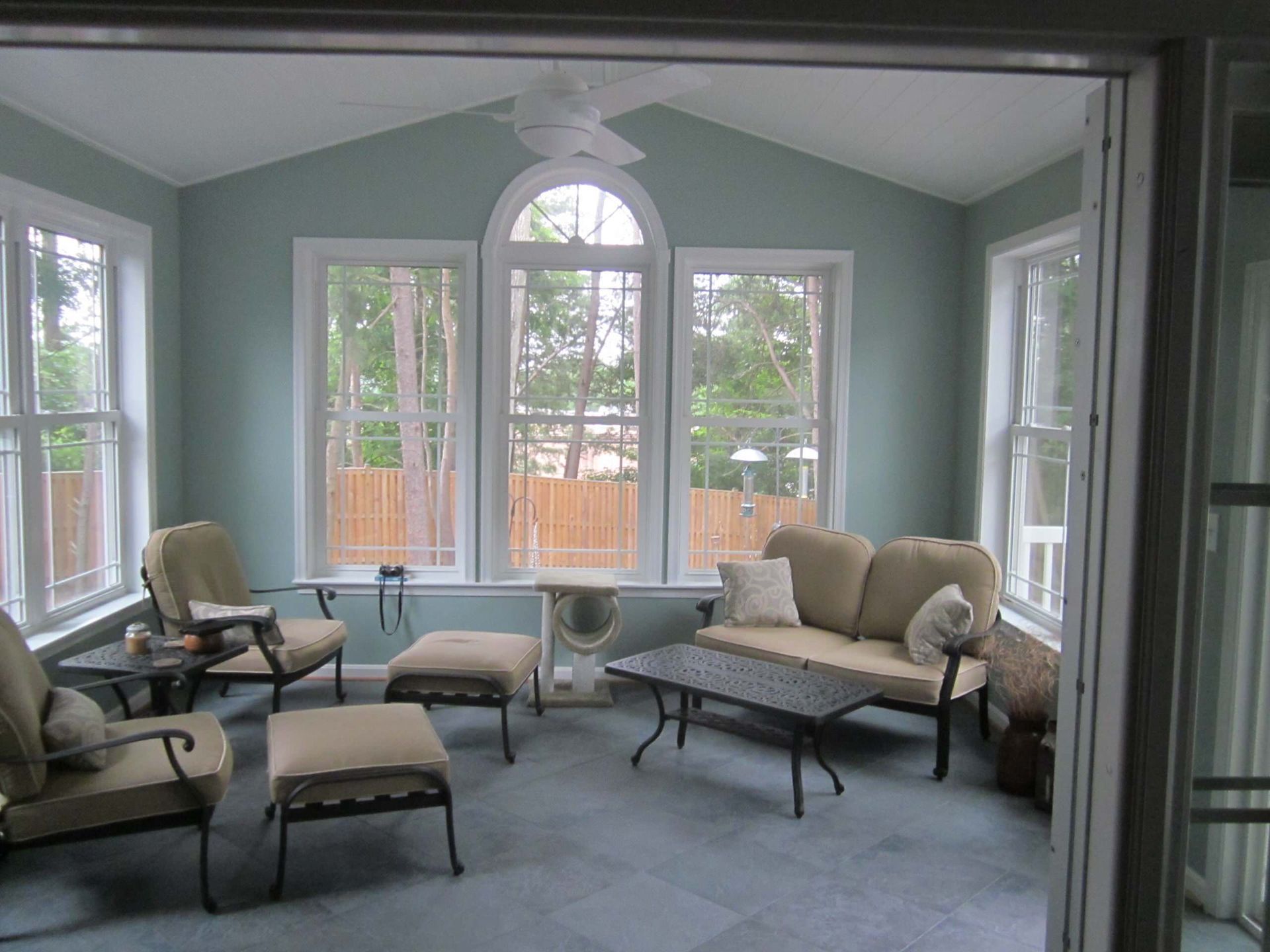 Bright living room with gray walls, large windows, and beige sofas and chairs around a central coffee table.