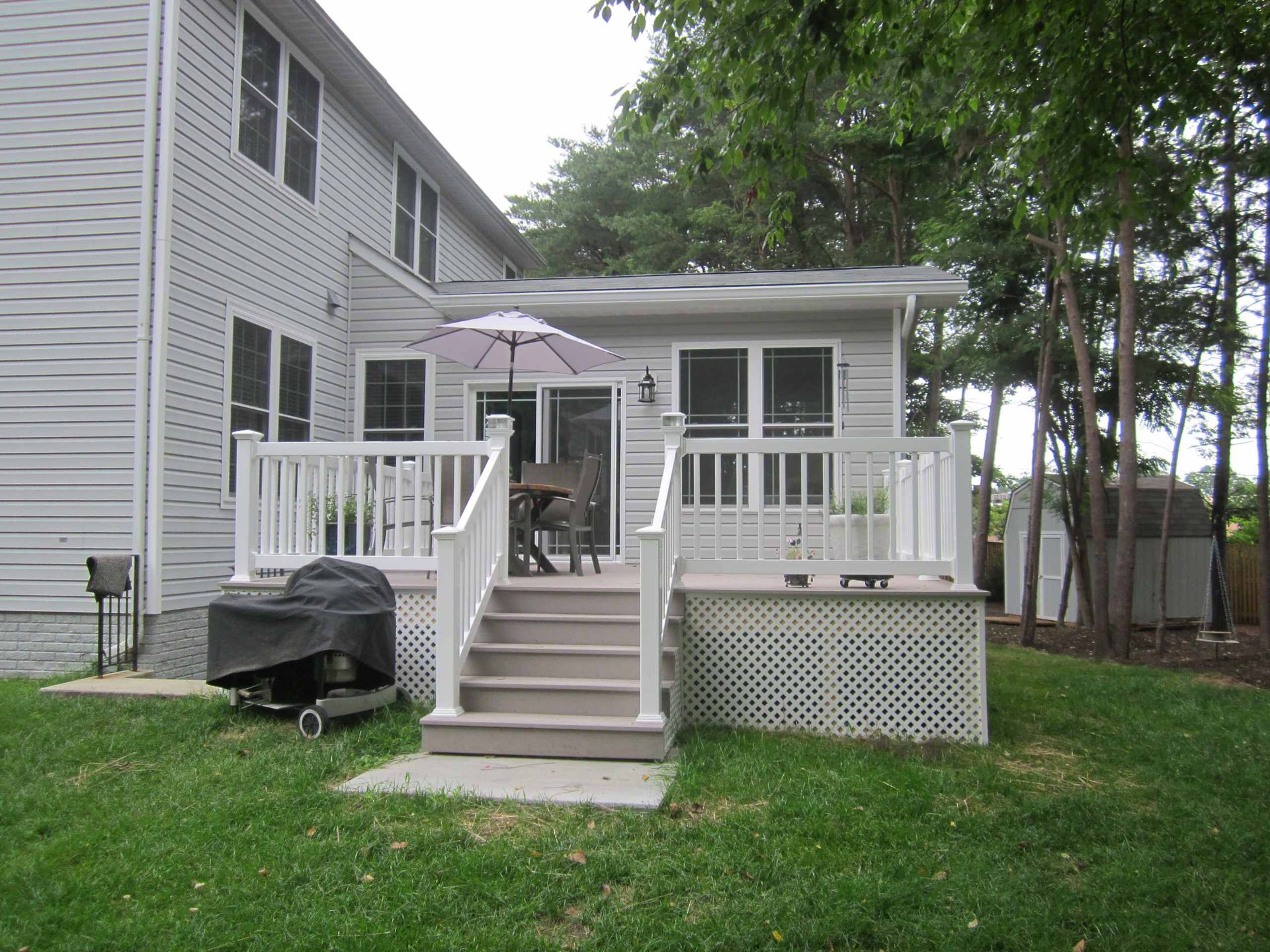 Backyard deck with white railing, steps, grill, and patio umbrella beside a house