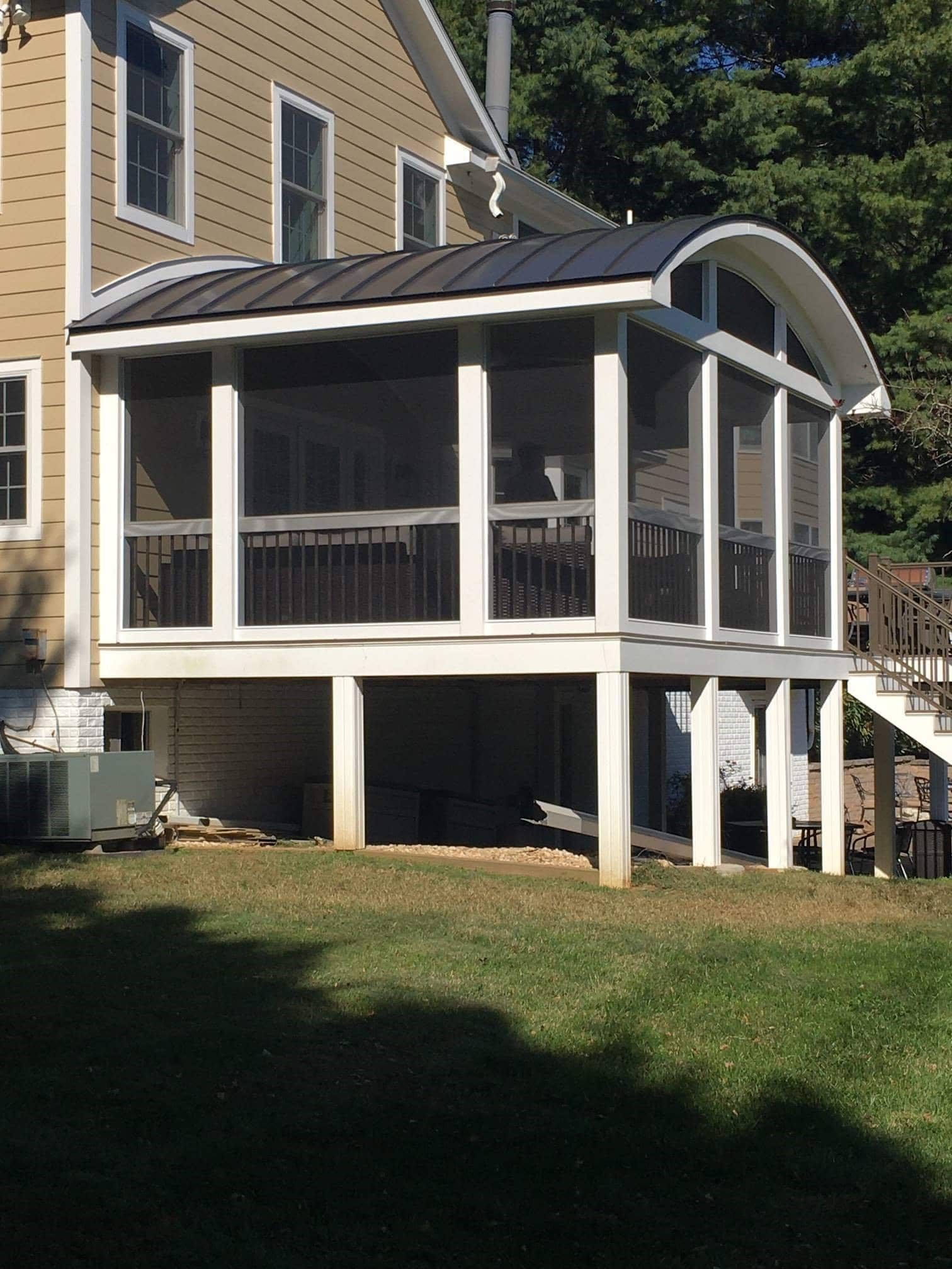 White screened porch with arched roof attached to a tan house, elevated above a grassy yard.