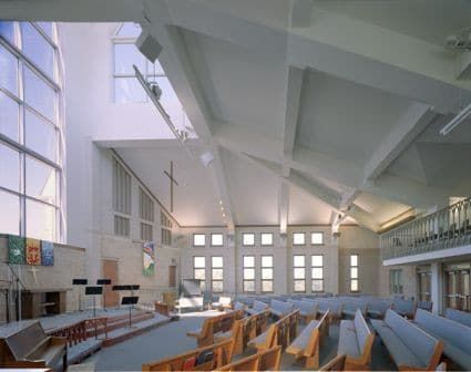 Bright modern church sanctuary with rows of blue chairs, wooden pews, and tall windows under a white vaulted ceiling